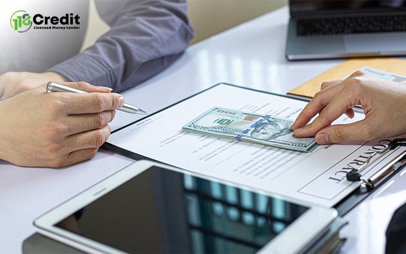 Two people at a table exchanging a $100 bill over a document labeled “CONTRACT,” with tech devices nearby.