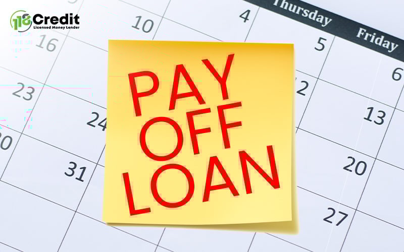 Yellow sticky note with bold red text “PAY OFF LOAN” placed on a calendar showing early-month dates.
