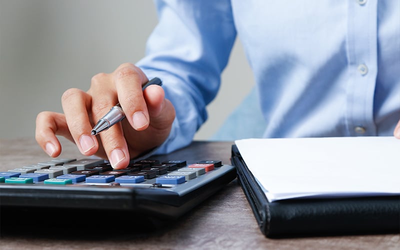Close-up of a person using a calculator and taking notes on a financial ledger.