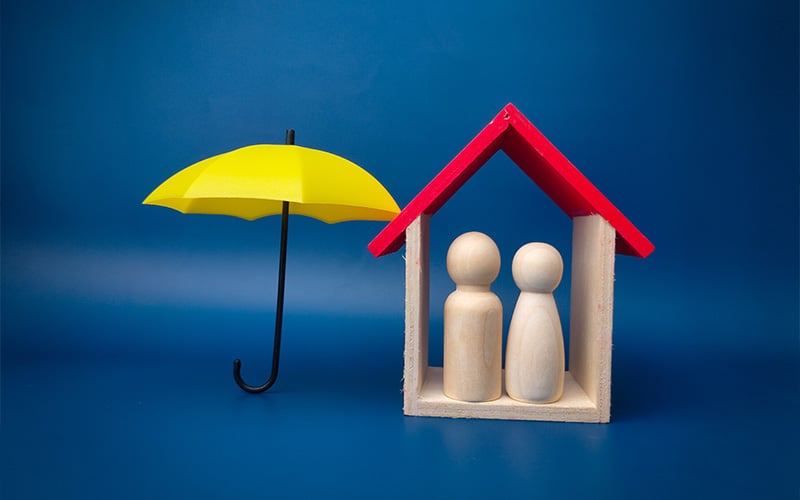 Wooden figures inside a toy house next to a yellow umbrella.