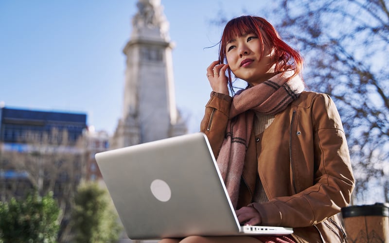 Freelancer using laptop outdoors while applying for loan approval.